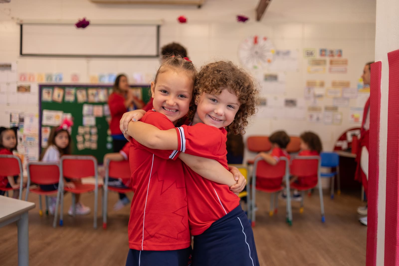 Crianças da Educação Infantil se abraçando e sorrindo no pátio da escola